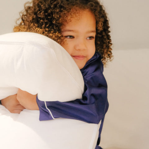 A young child smiling and holding a Slumber Cloud Core Down Alternative Pillow