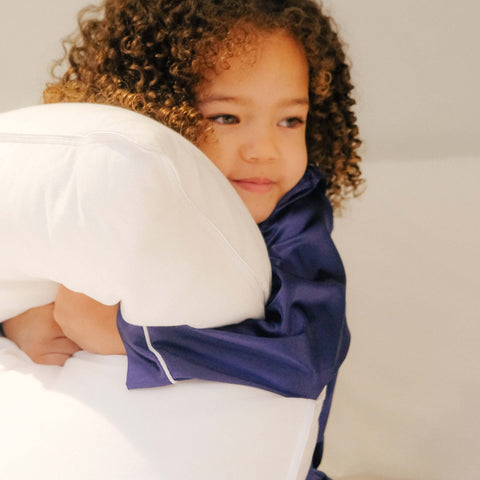 A young child smiling and clutching a Slumber Cloud Core Down Alternative Pillow