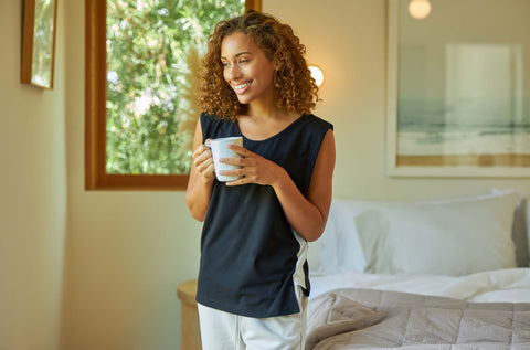 A young woman smiling and holding a cup of coffee while wearing a Slumber Cloud UltraCool Tank