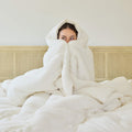 A young woman wrapped in an Avec Goods Cotton Quilt while sitting on a bed
