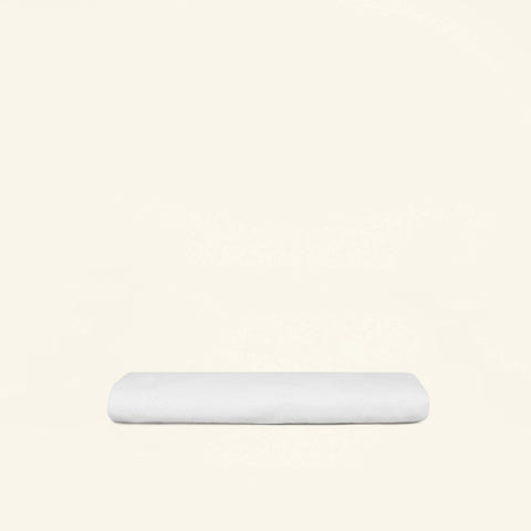 A folded Slumber Cloud Core Mattress Protector - Crib on a cream background