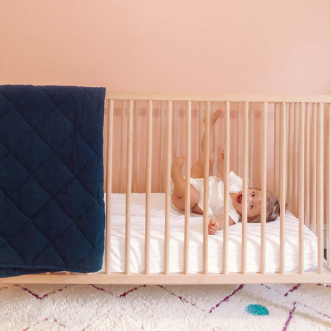 A baby in a crib lying on a Slumber Cloud Essential Fitted Sheet - Crib