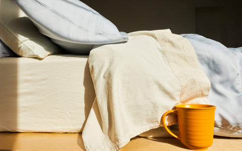 A sideview of a bed made with the Slumber Cloud Essential Duvet Cover and a cup of coffee sitting next to the bed
