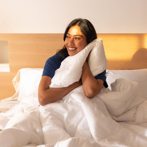 A young woman holding a Slumber Cloud UltraCool Comforter to her face while sitting in bed.