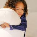 A young child smiling and holding a Slumber Cloud Core Down Alternative Pillow