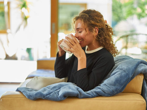 A young woman smiling and drinking coffee on a leather couch.